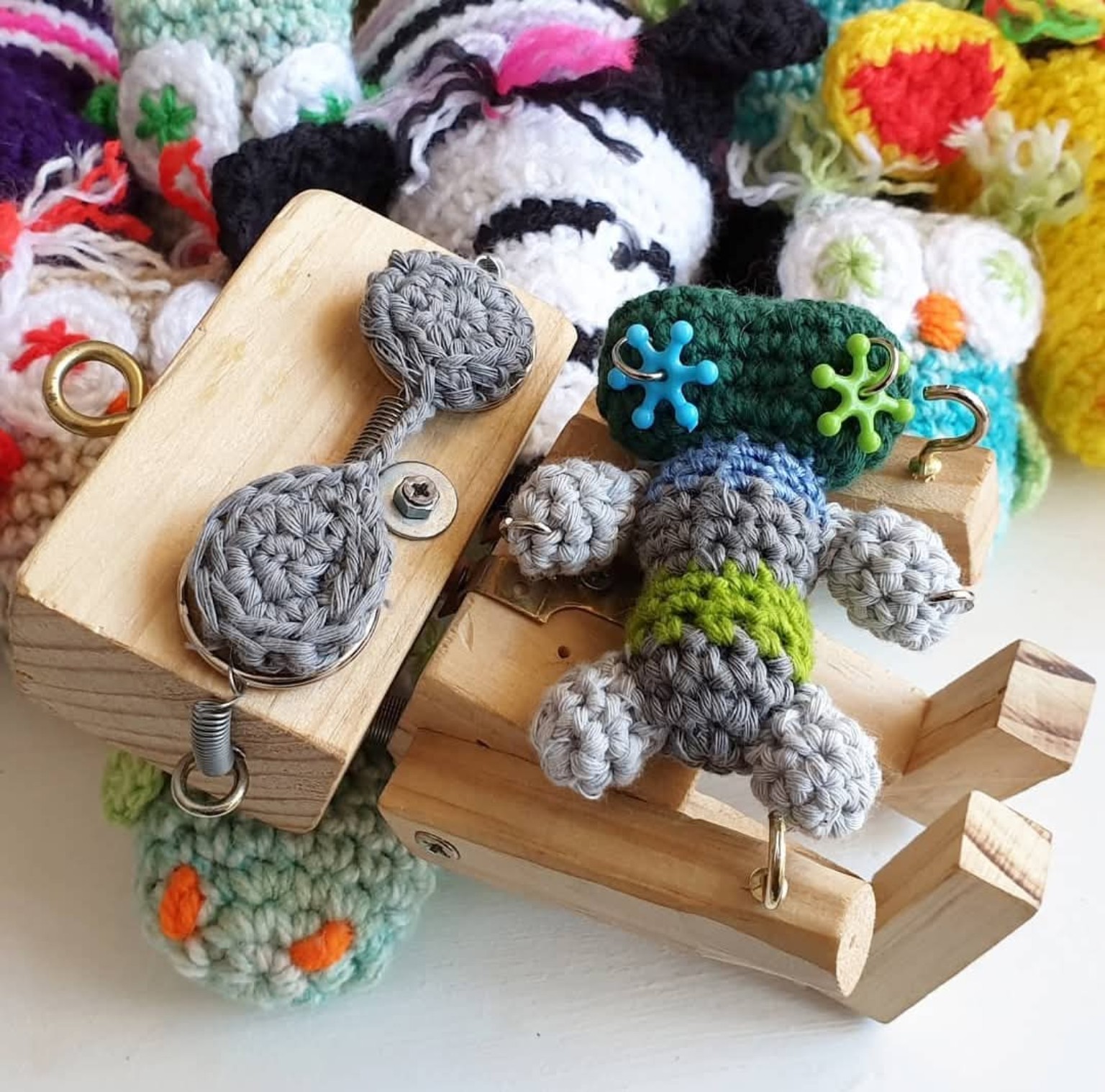 Wooden robot parts combined with crocheted grey and green pieces, surrounded by colourful crocheted characters