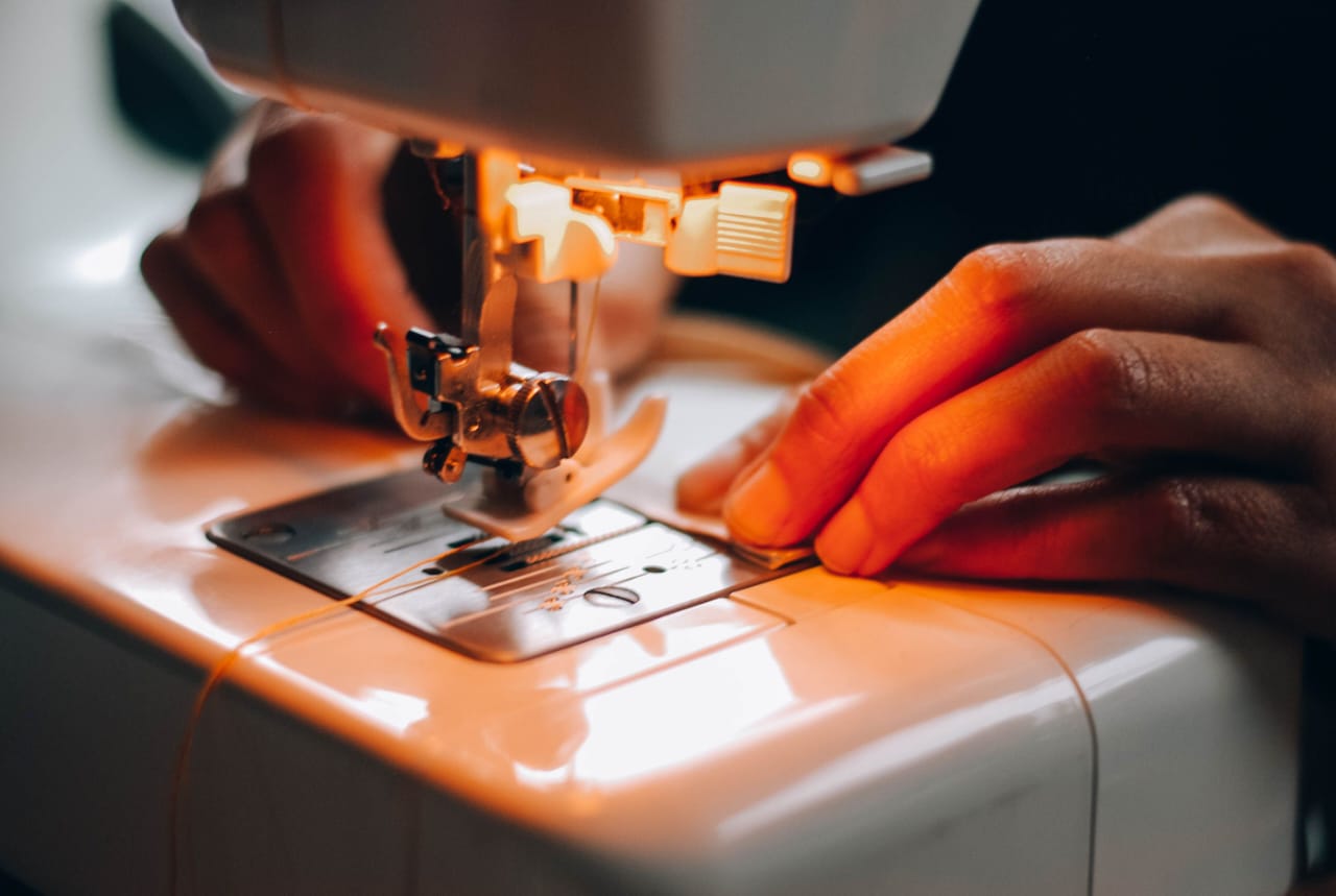 Hands guiding fabric through a sewing machine under warm light