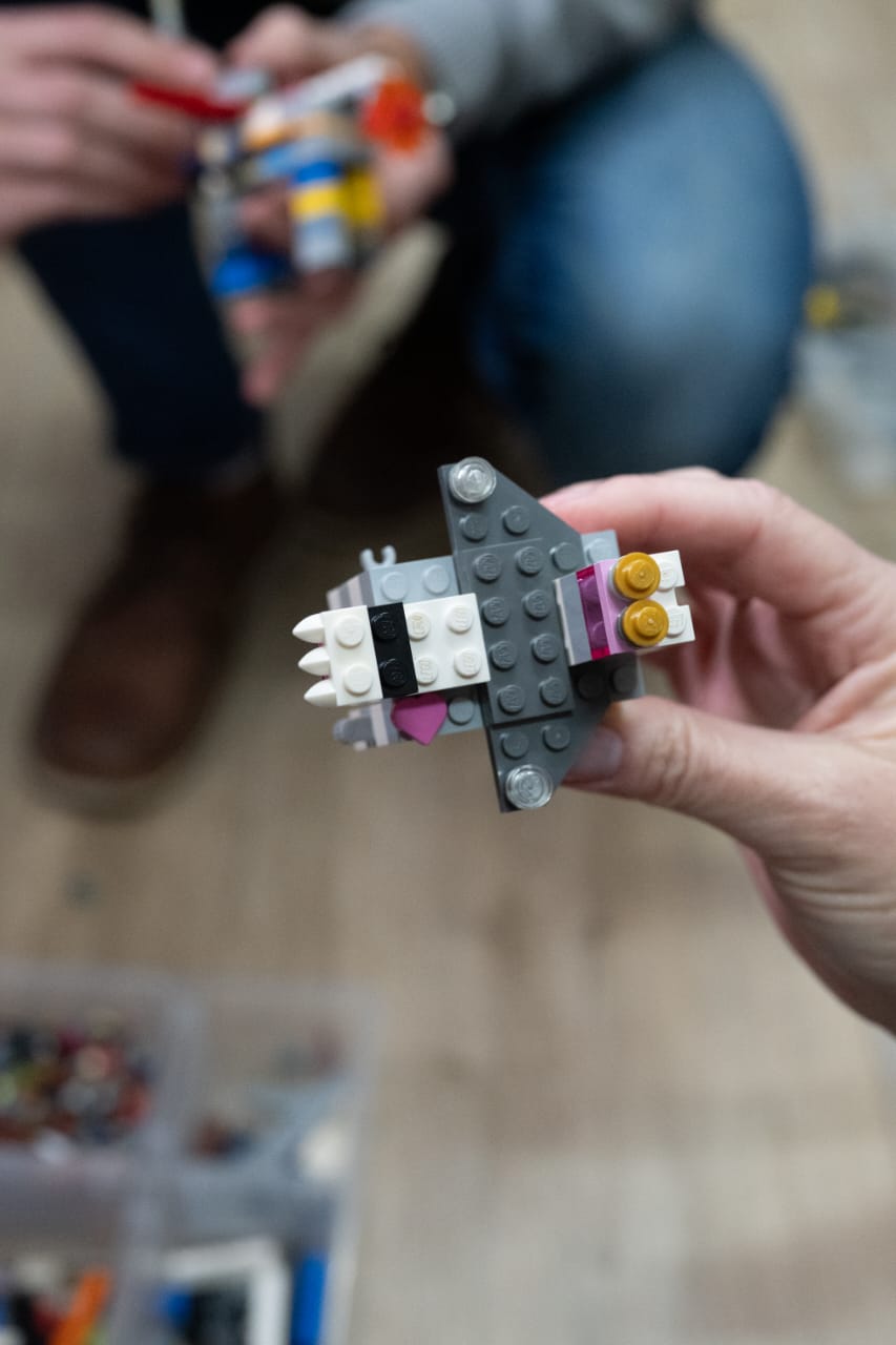 Hands holding a small brick model built during a facilitated team discovery session.