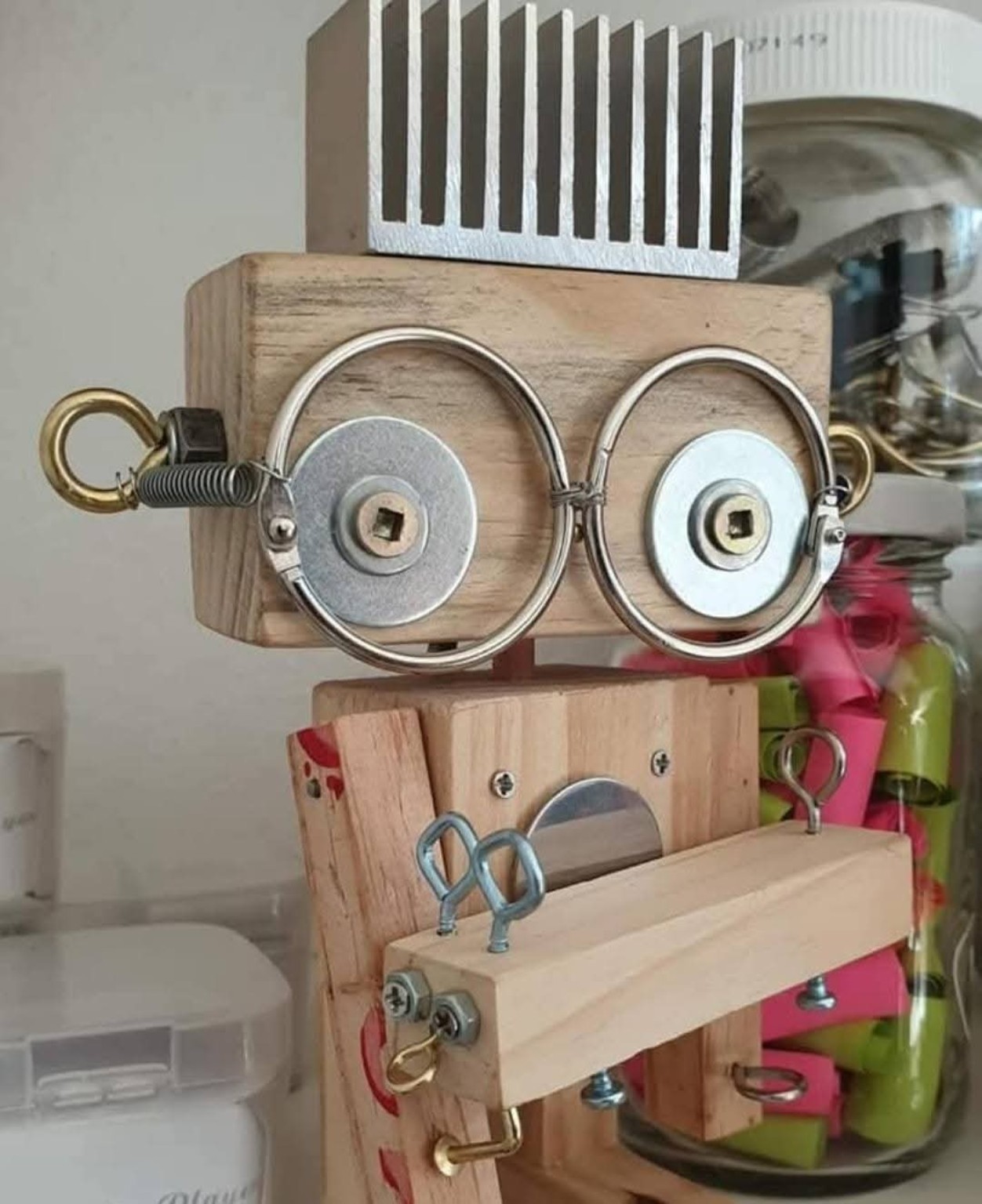 Close-up of a wooden robot head with a metal heat sink for hair and large ring-and-disc eyes