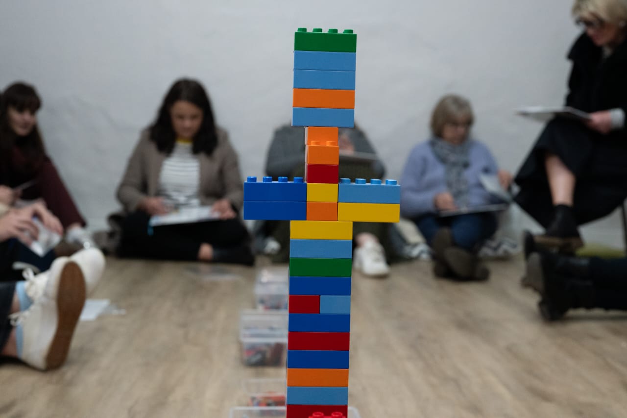 A tall, colourful brick tower standing in front of a corporate team seated in discussion.