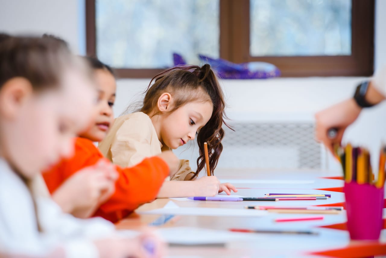 Children drawing with pencils at a table covered in paper and coloured pencils