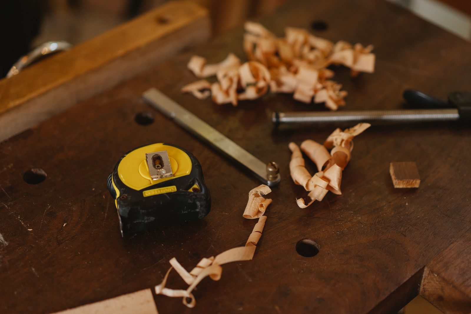 A tape measure, steel rule and curls of wood shavings on a dark workbench
