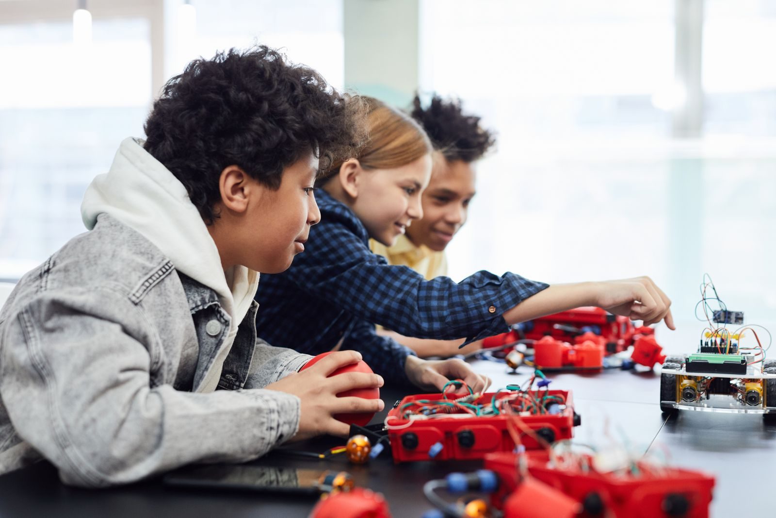 Three young people leaning over a table, building a wheeled machine together
