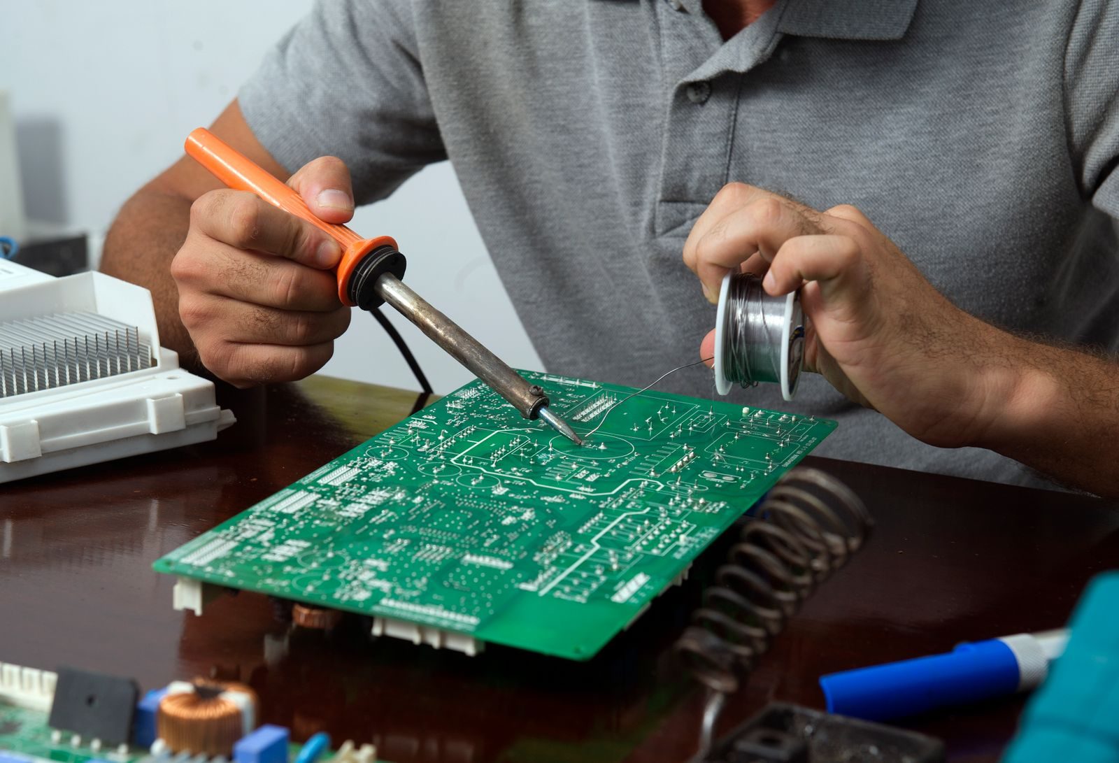 Close-up of a soldering iron being used on a green circuit board