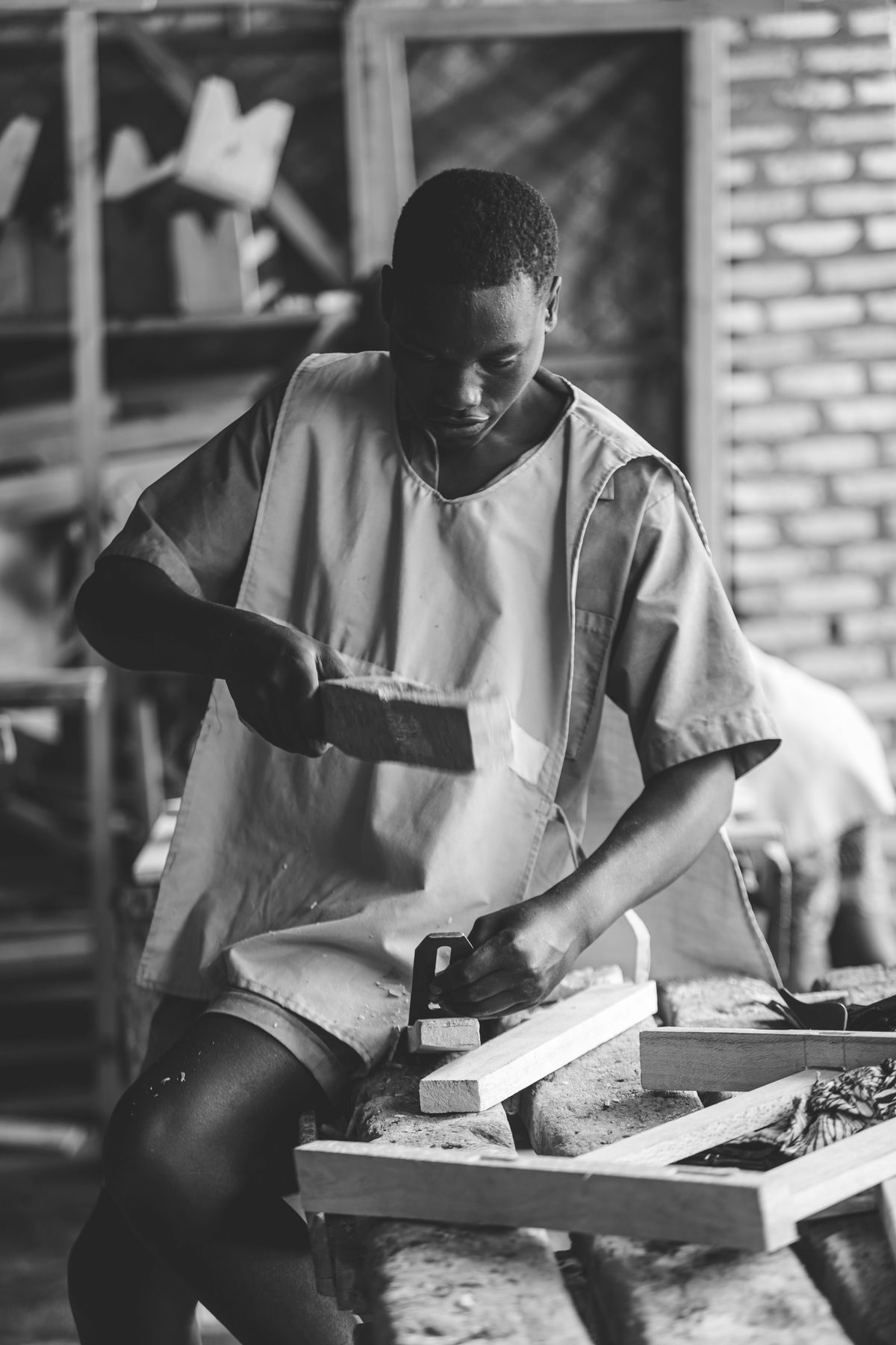 Black and white photograph of a young carpenter shaping wood at a bench